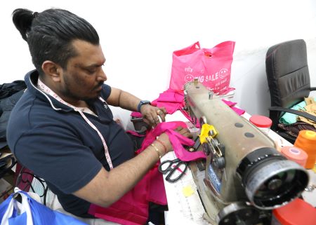 Man sewing pink cloth on sewing machine