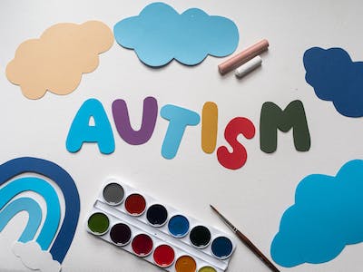 Image of the word Autism  surrounded by crayoins and cut-out clouds.
