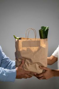 Groceries in a brown bag being passed on to someone
