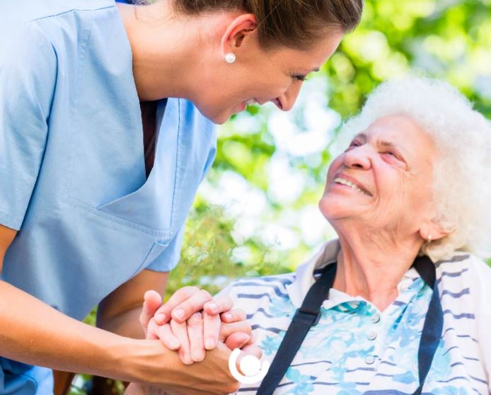 Adult social care woman smiling at older lady in wheelchair