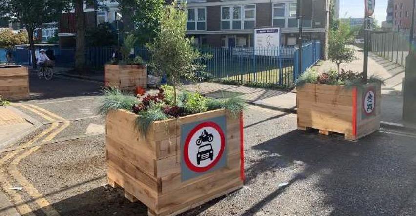 Image of  square planters made our of wood with plants inside, used to block a section of the road so vehicles can't get through